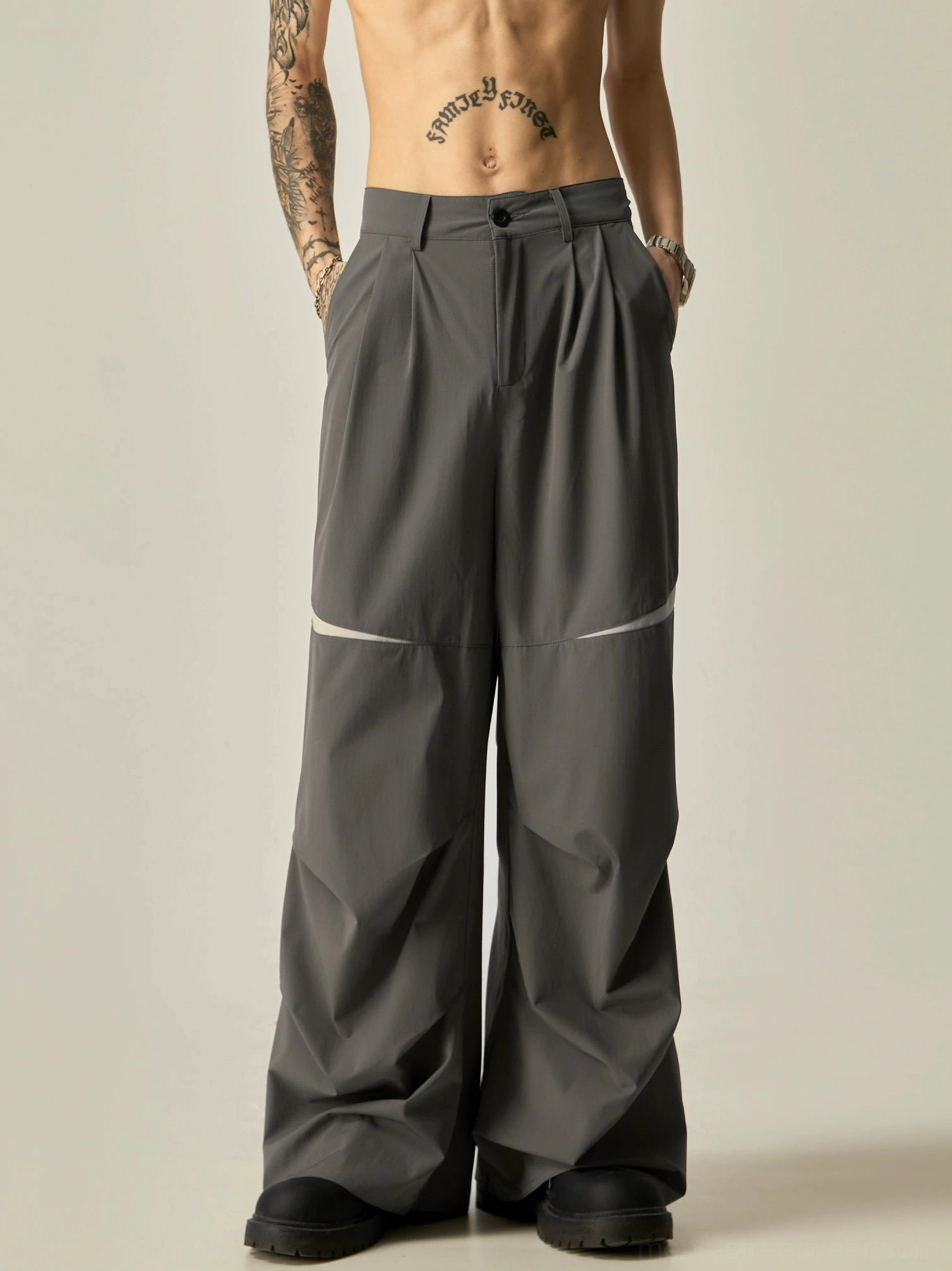 Dark gray oversized track pants with curved knee detailing, pleated high waist, smooth fabric, and side pockets