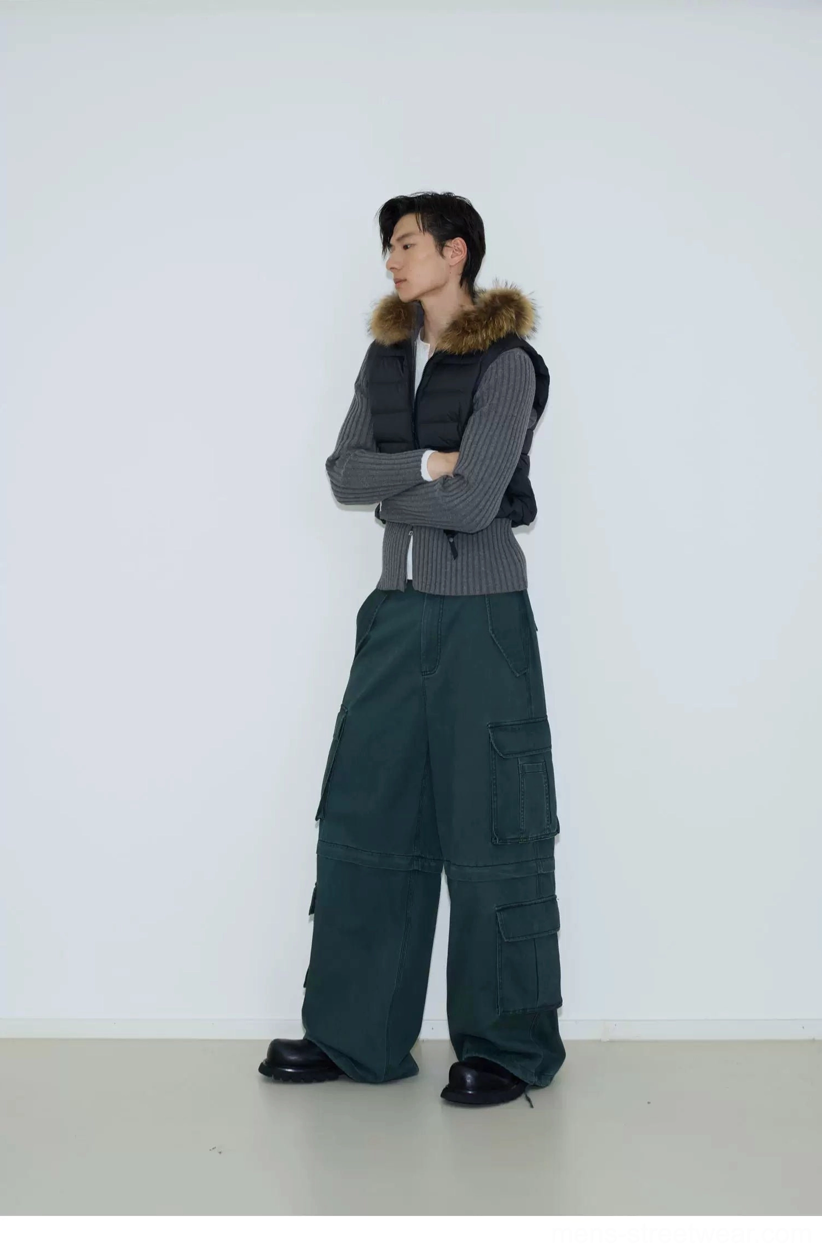 Dark grey quilted cropped puffer vest layered over knitwear with green cargo pants in a streetwear studio look