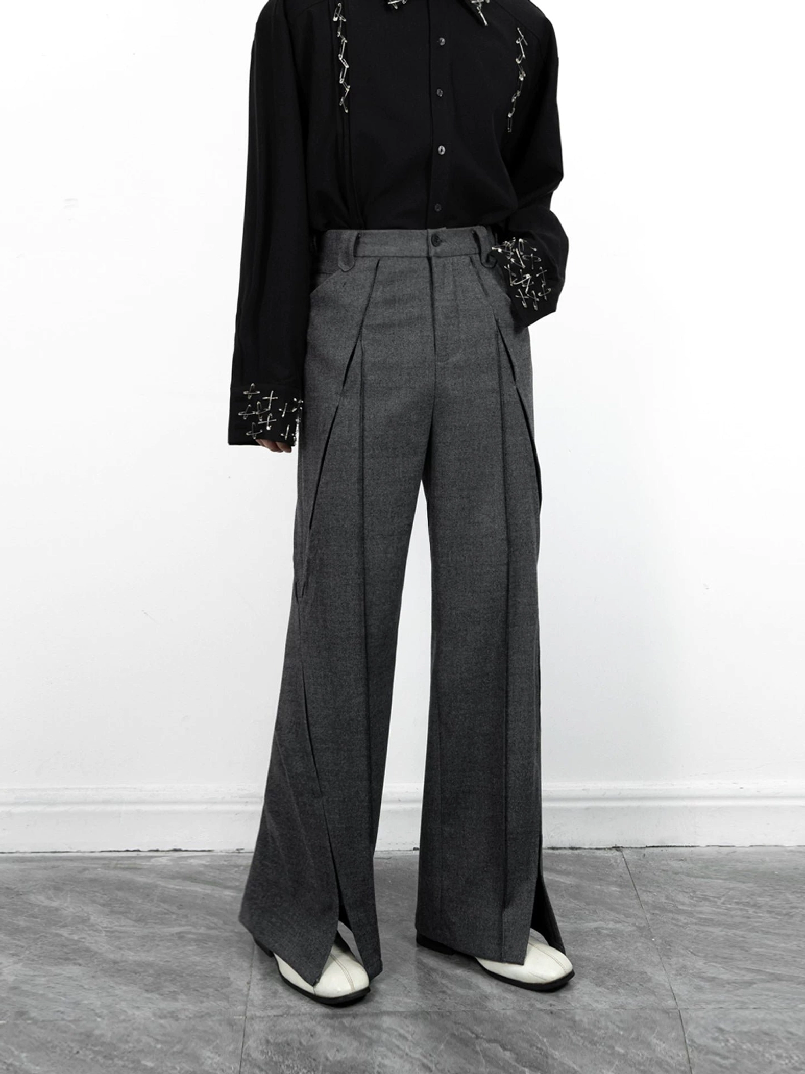 Front view of dark grey split-hem wide-leg trousers featuring tailored front pleats, side pockets, and a structured suiting silhouette