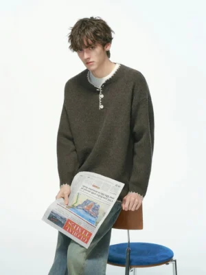 Men's dark heather brown henley knit sweater with contrast trim and decorative buttons styled with blue jeans in a minimalist studio