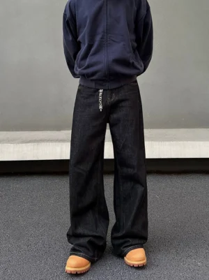 Front full-body view of dark indigo wide leg streetwear jeans with metal chain waist detail and stacked hems