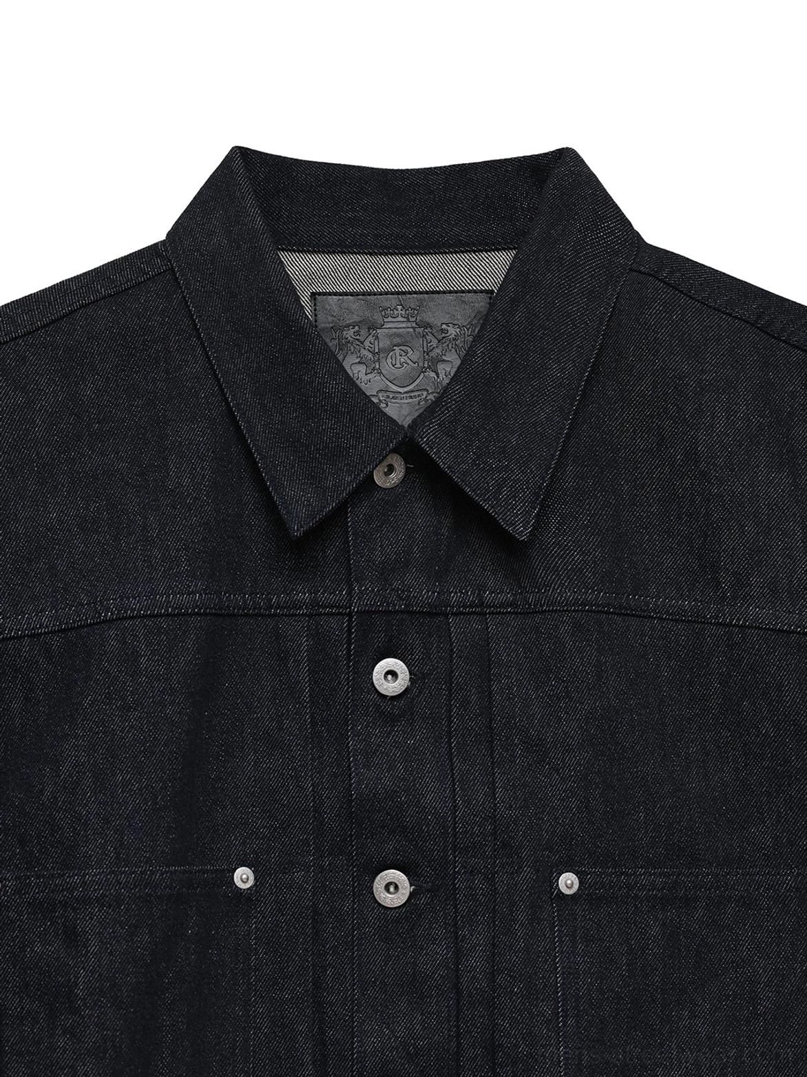 Close-up of dark indigo denim jacket pointed collar metal snap buttons and textured twill fabric