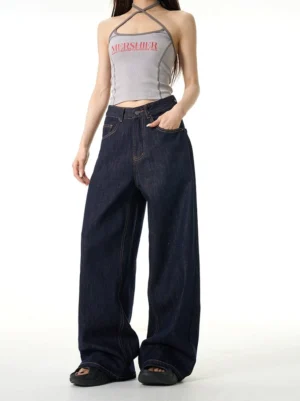 Female model wearing dark indigo mid-rise wide-leg jeans with contrast stitching in a white studio front view