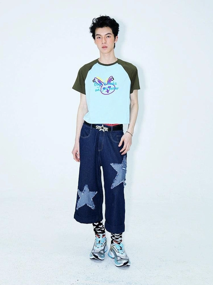 Full front view of dark indigo star appliqué denim culottes worn with a color block raglan cropped tee, patterned socks, and sneakers