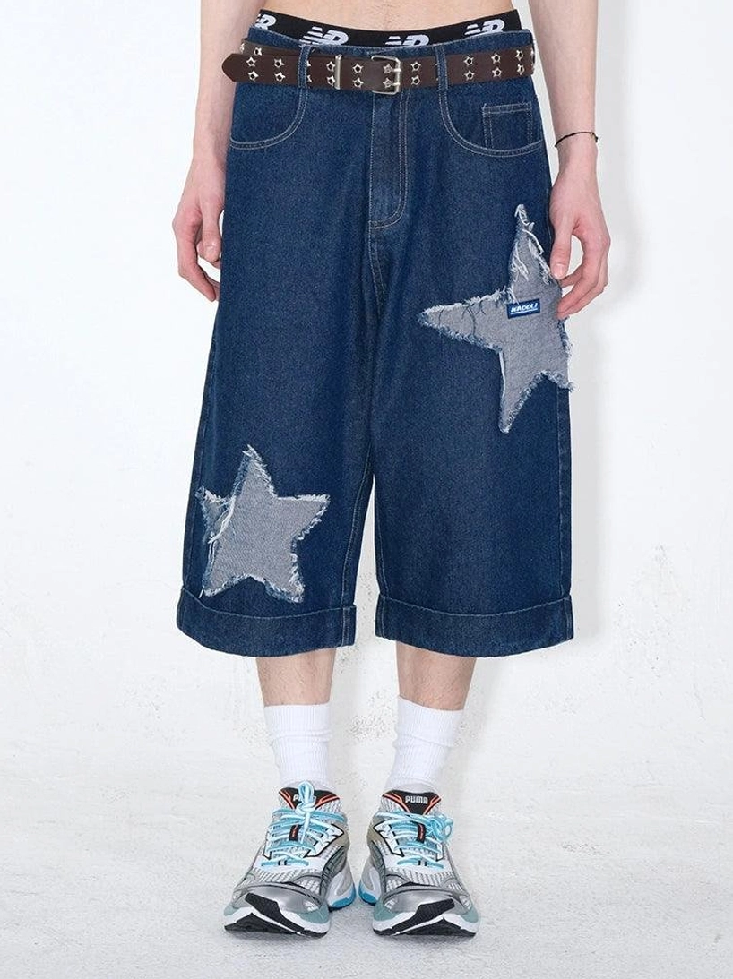 Front close-up of dark indigo star patch denim culottes with cropped wide-leg silhouette, frayed grey appliques, brown leather belt, white socks, and retro sneakers