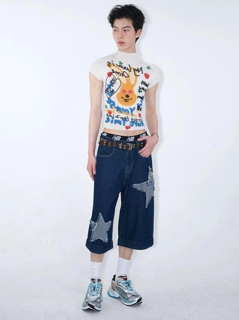 Male model wearing dark indigo cropped wide-leg denim culottes with frayed star patches, brown belt, graphic white tee, and sneakers