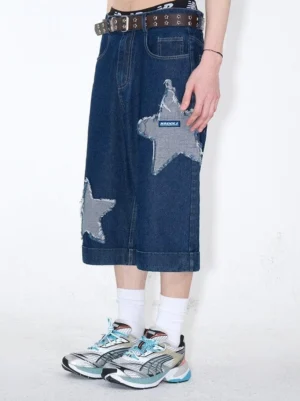 Side view of dark indigo denim culottes featuring frayed grey star patches, cropped wide-leg cut, back pocket details, white socks, and silver blue sneakers