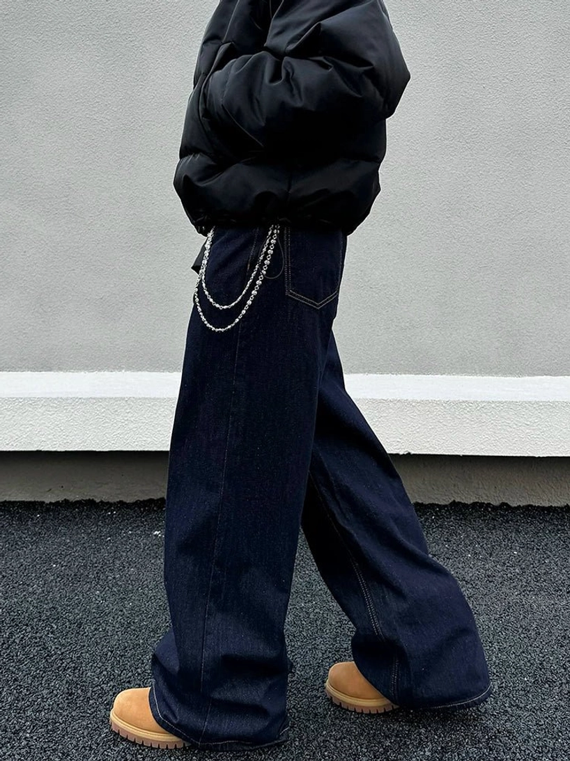Side profile of relaxed dark indigo wide-leg denim jeans with a layered waist chain and black puffer jacket in Seoul-inspired streetwear styling