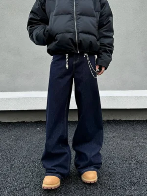Front view of dark indigo wide-leg jeans with layered metal waist chains, black zip-up puffer jacket, and tan work boots