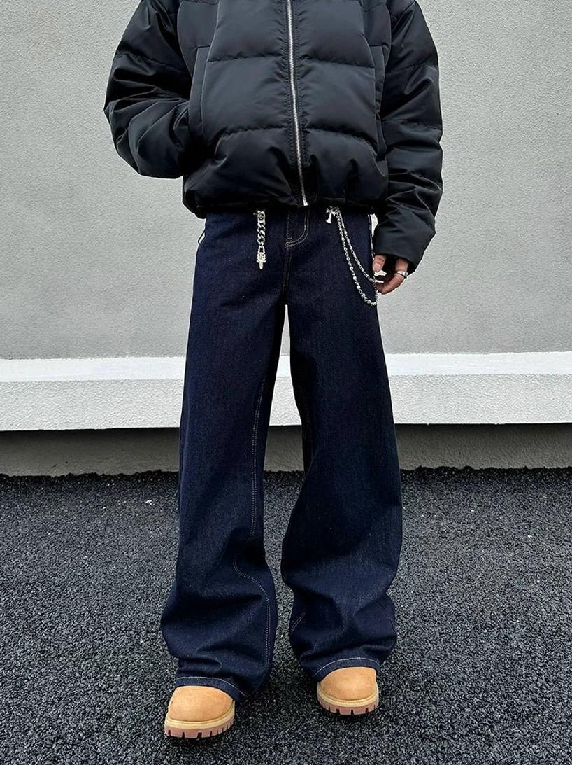 Front view of dark indigo wide-leg jeans with layered metal waist chains, black zip-up puffer jacket, and tan work boots