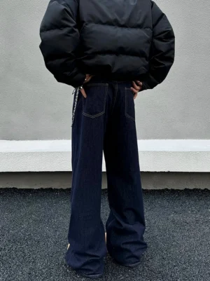 Back view of dark indigo wide-leg streetwear jeans styled with a black cropped puffer jacket, metal waist chain, and stacked hem on a rooftop
