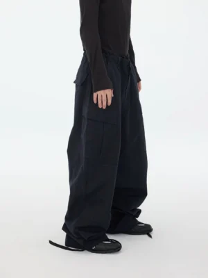 Right side view of oversized dark navy cargo pants showing relaxed wide-leg proportions, utility side pockets, waist drawstring, and adjustable gathered hems