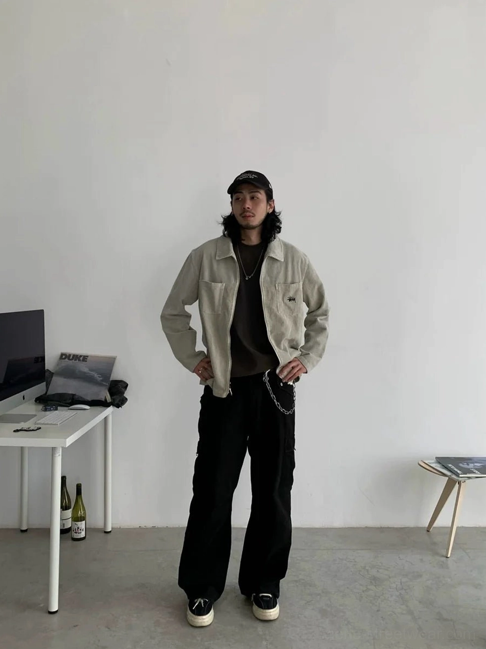 Front view of dark neutral straight leg cargo pants with pant chain detail styled with a light khaki cargo jacket and black inner tee