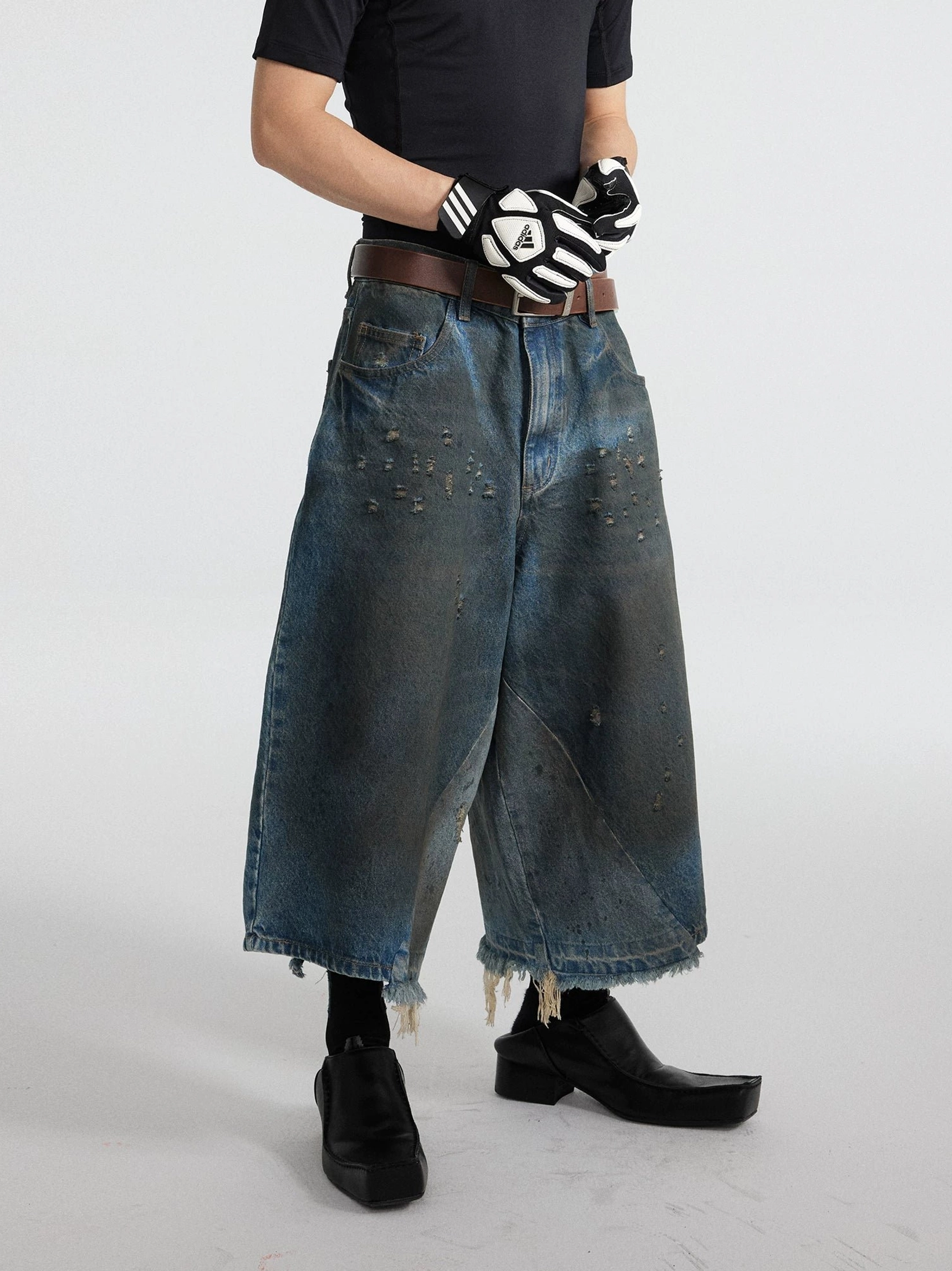 Three-quarter side view of dark oil-washed distressed wide-leg cropped gaucho jeans with faded denim texture, raw hems, and oversized streetwear fit