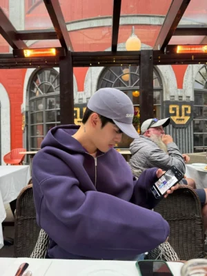 Dark purple oversized double-zip hoodie with dropped shoulders and wide sleeves styled at an outdoor cafe in a modern Seoul streetwear look
