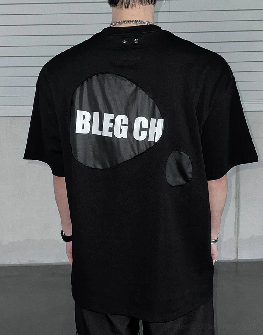 Back view of oversized black street tee featuring large irregular contrast graphic patch and exposed neckline stitching