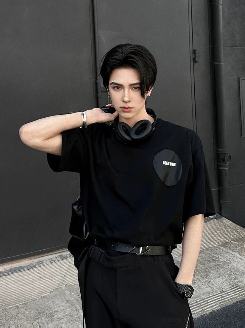 Oversized black graphic street tee with small chest patch paired with cargo pants and crossbody bag