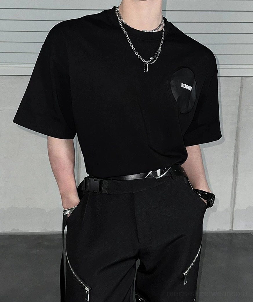 Close-up of black oversized graphic tee chest patch with zipper cargo pants leather belt and chain necklace