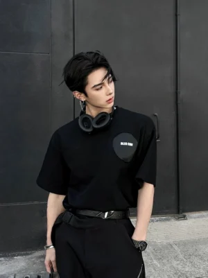 Front view of oversized black street tee with subtle chest patch styled in an industrial urban setting