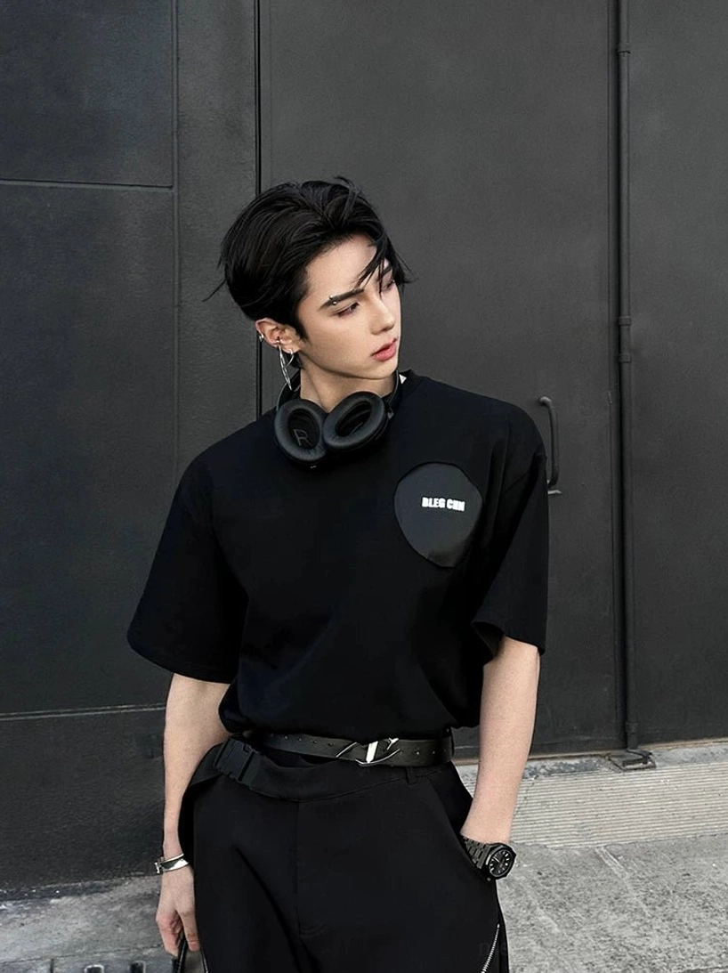 Front view of oversized black street tee with subtle chest patch styled in an industrial urban setting