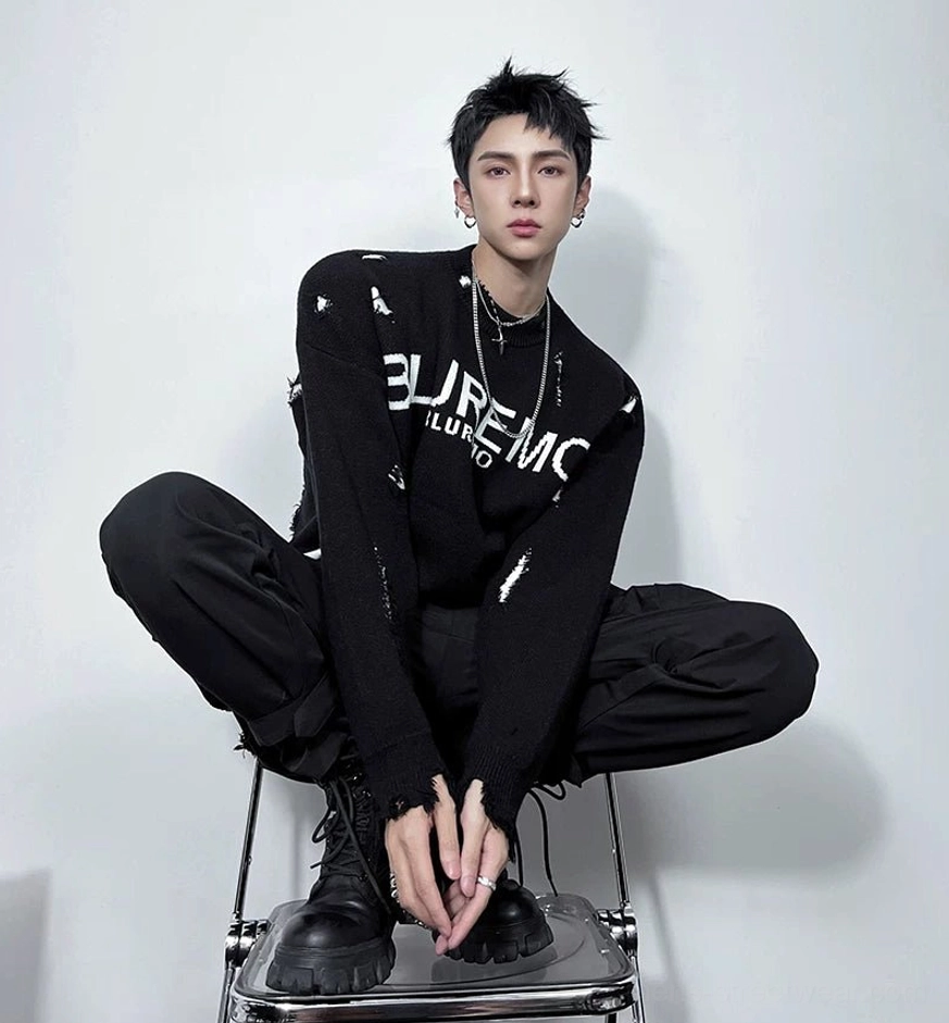 Low-angle view of a black deconstructed shred-knit sweater with distressed chest lettering, frayed cuffs, ripped details, and relaxed streetwear fit