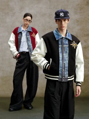 Two models wearing black and claret denim panel embroidered varsity bomber jackets with striped ribbed trims in a vintage studio setting