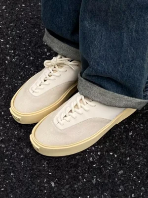 Desert Gray low-top platform canvas trainers worn with rolled dark blue denim jeans on gravel pavement