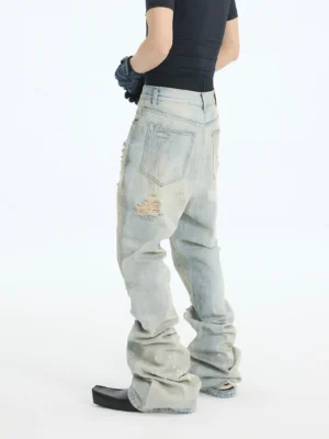 Side rear view of dirty blue distressed stacked flare jeans showing pooled hems, ripped thighs, and acid wash denim