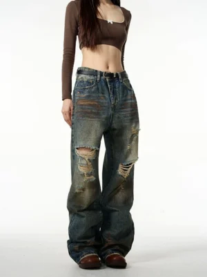 Front view of distressed baggy ripped jeans in faded vintage blue denim styled with a brown cropped top and leather loafers