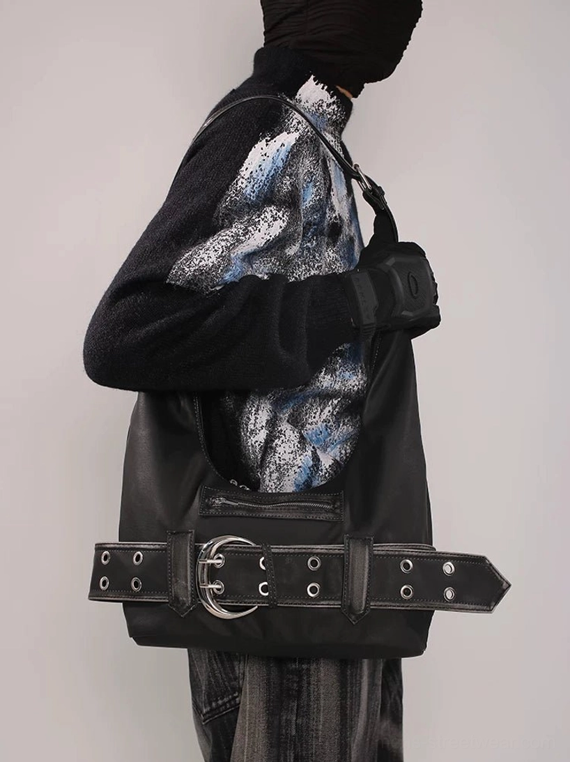 Black distressed buckle belt hobo bag worn under the arm with dark Seoul streetwear outfit, showing grommet hardware and front zip pocket