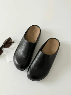 Distressed black closed-toe mule clogs with rounded leather-look upper and tan insole shown from an angled top view
