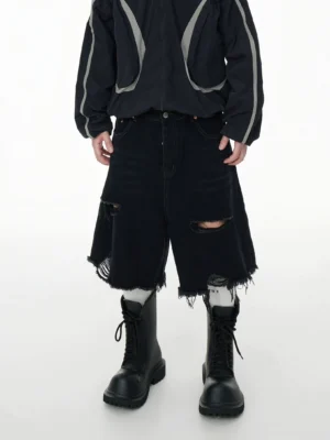 Rear low angle view of oversized distressed black denim jorts with ripped panels, frayed raw hems, classic back pockets, and combat boots in a streetwear outfit