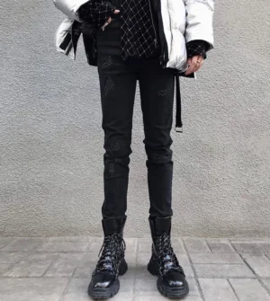 Distressed black skinny jeans with hanging side strap styled with silver puffer jacket and chunky black martin boots in industrial Seoul streetwear look