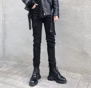 Male model wearing distressed black stacked skinny jeans with ripped knees, black leather jacket, and chunky platform combat boots in an urban streetwear setting