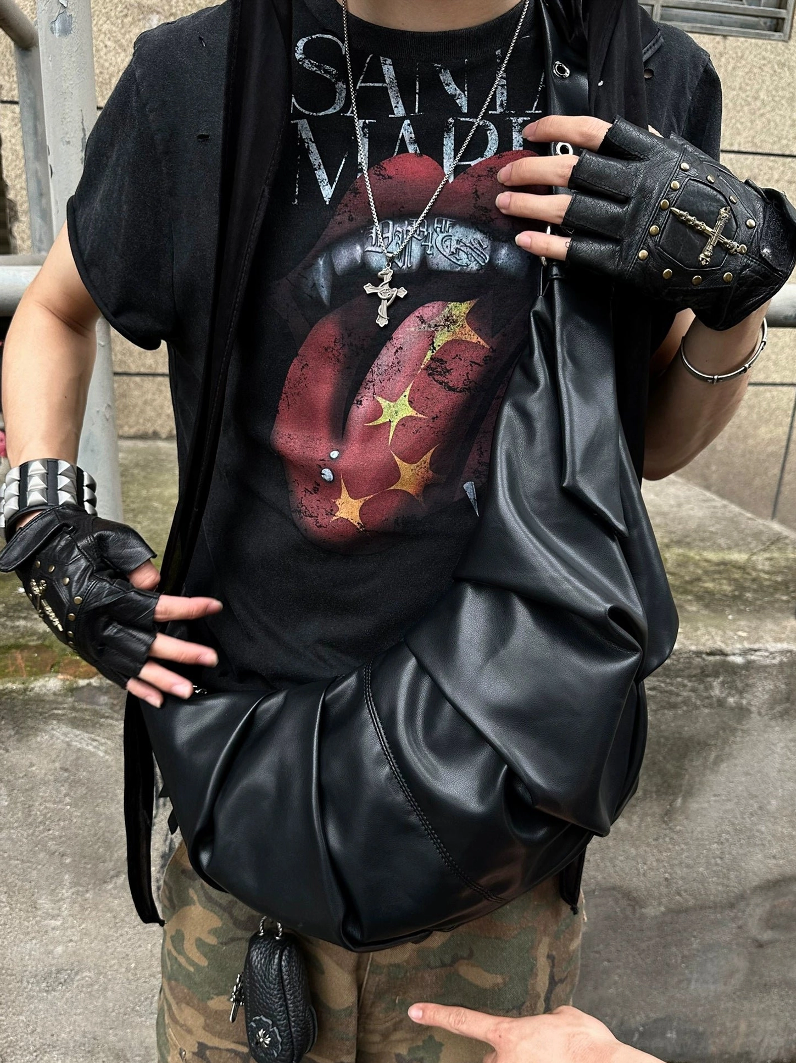 Close-up of distressed black vampire tongue graphic T-shirt styled with cross necklaces and leather streetwear accessories