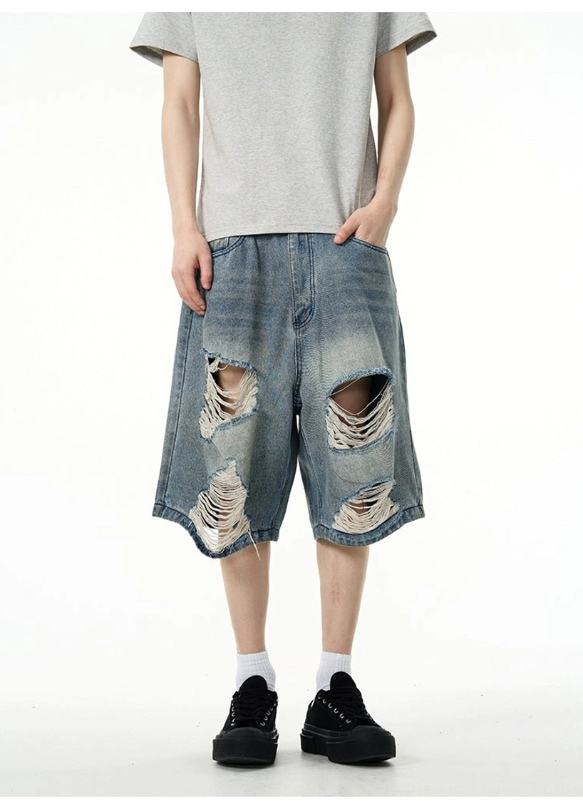 Partial torso and lower-body view showing distressed blue denim Bermuda shorts styled with a grey short-sleeve T-shirt, black socks, and loafers
