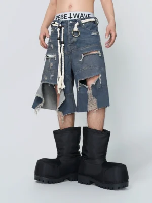 Front view of distressed blue denim shorts with oversized ripped panels, frayed edges, wide legs, white rope belt, and metal ring detail