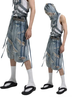 Side and front view of relaxed distressed denim Bermuda shorts with harness-inspired straps, shredded panels, and loose streetwear fit