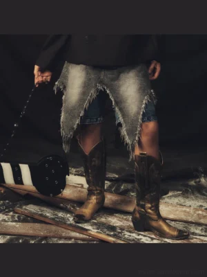 Distressed denim chaps with asymmetric frayed fringe hem styled over blue denim shorts with cowboy boots