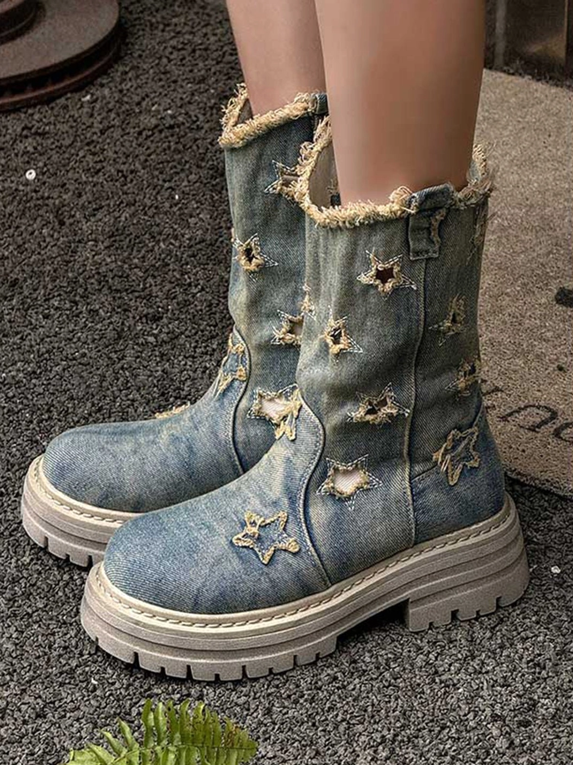 Front three-quarter model view of distressed blue denim star cutout platform boots with thick grey rubber lug soles