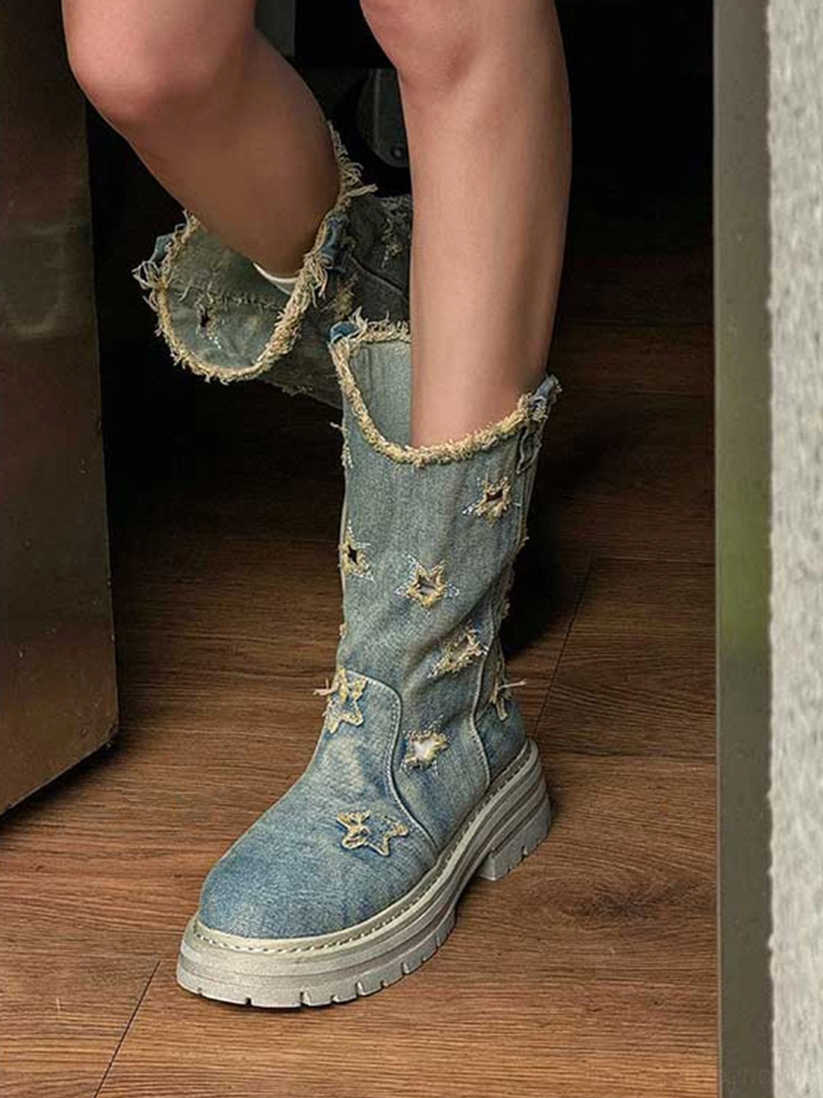 Top-down indoor view of model wearing washed blue distressed denim star platform boots with frayed cuffs and grey lug soles
