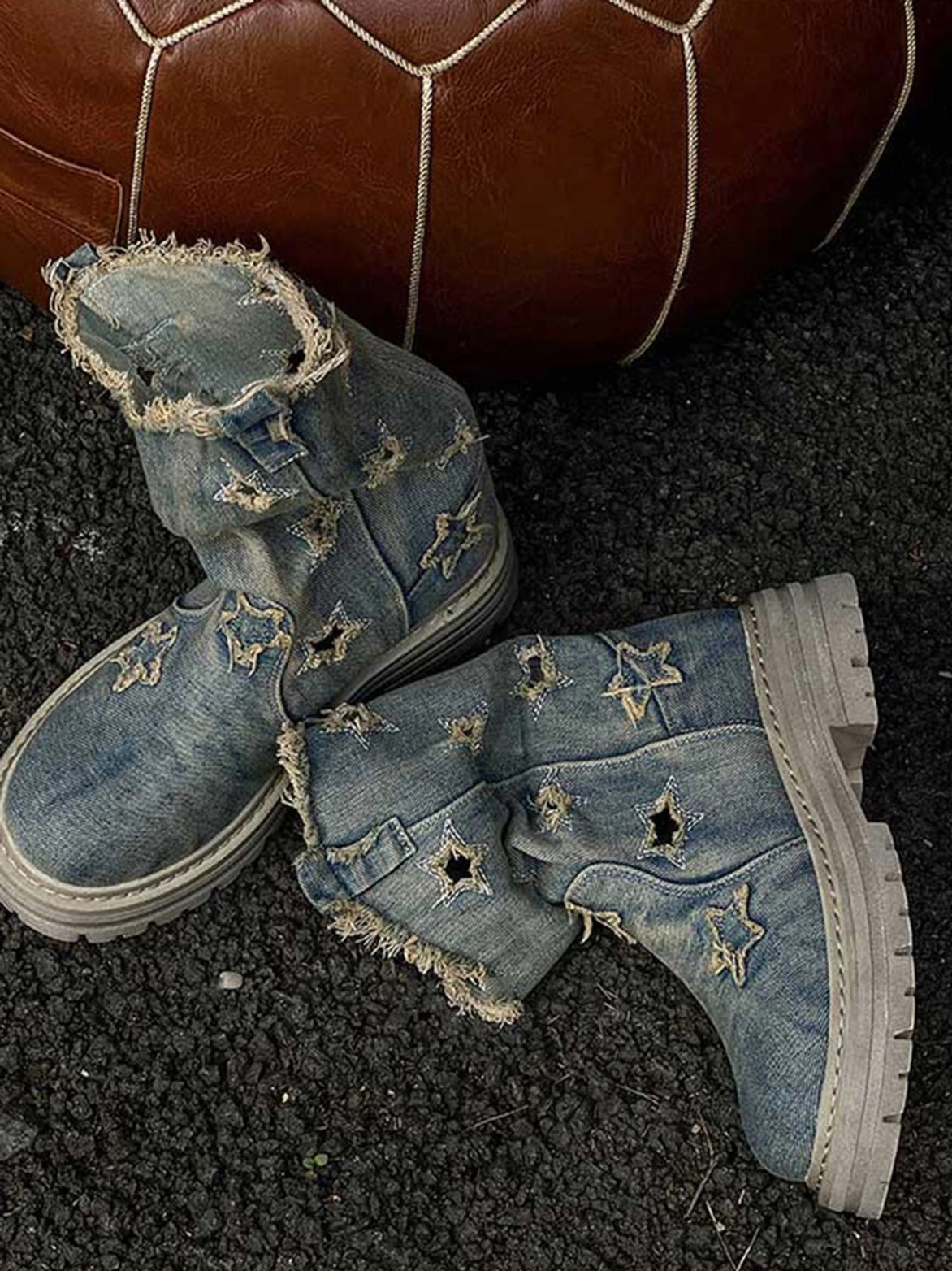 Outdoor overhead view of distressed denim star cutout platform boots with faded blue uppers and thick grey lug soles