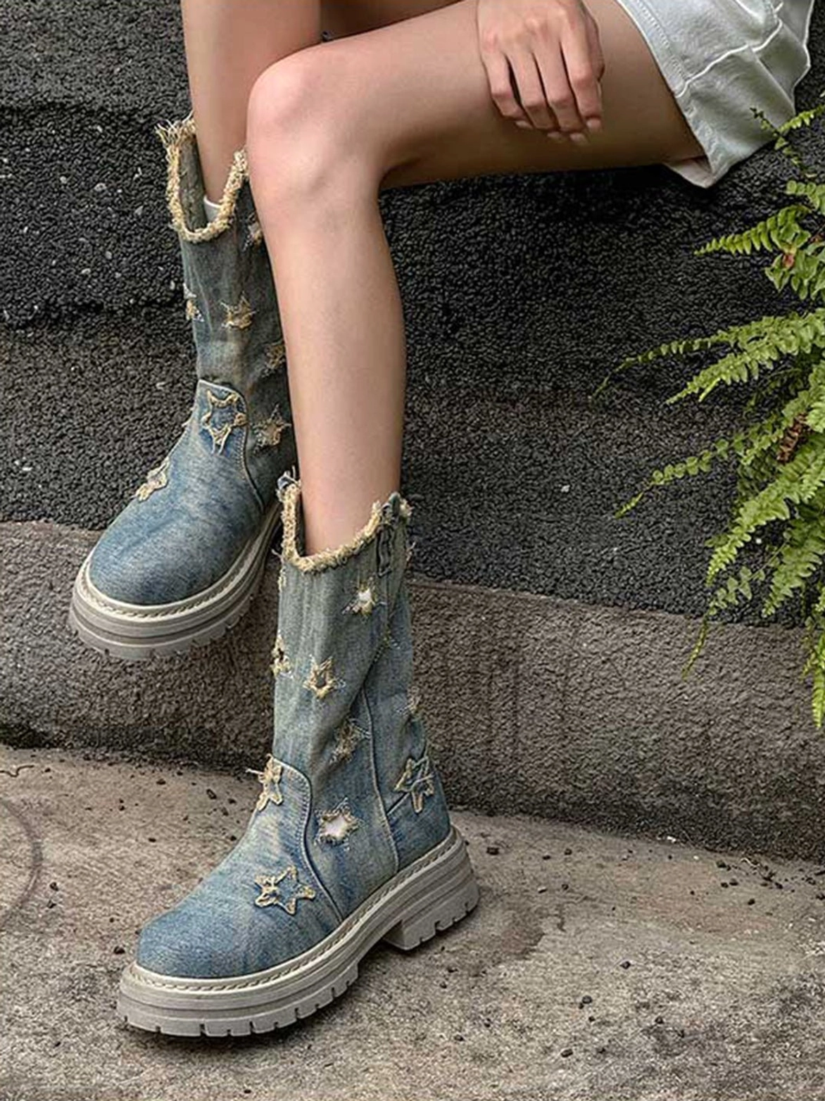 Outdoor side view of distressed denim star cutout mid-calf platform boots worn with a streetwear outfit on stairs