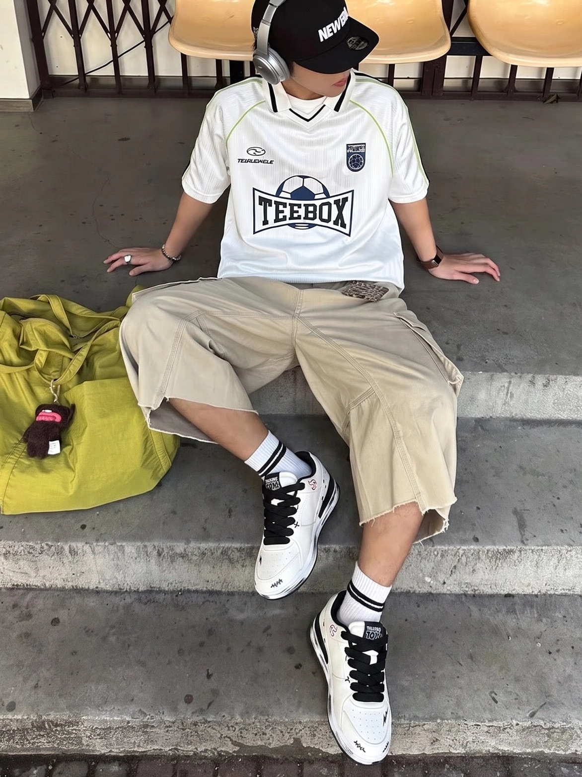 Distressed flame graphic court sneakers worn with a football jersey, cargo shorts, cap, and headphones on concrete stairs
