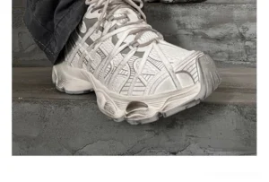Single distressed gray chunky sneaker shown in side three-quarter view on concrete stairs with layered panels and wraparound laces