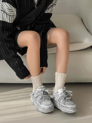 Distressed gray thick-soled platform sneakers worn with beige ribbed socks and a black knit outfit in a casual indoor setting