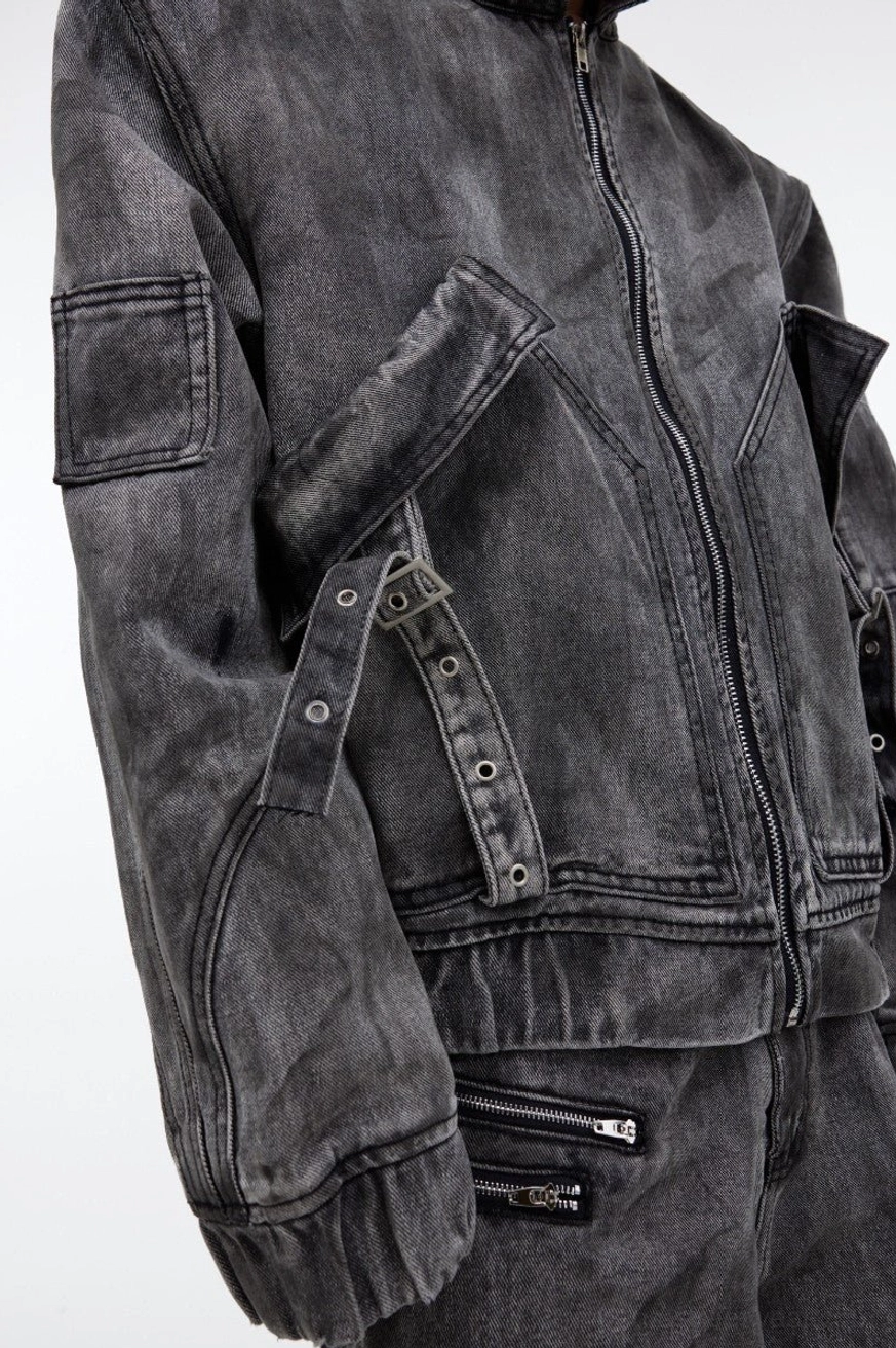 Close-up of distressed gray utility denim jacket with metal snap buckle chest pocket straps sleeve zip pocket and washed texture