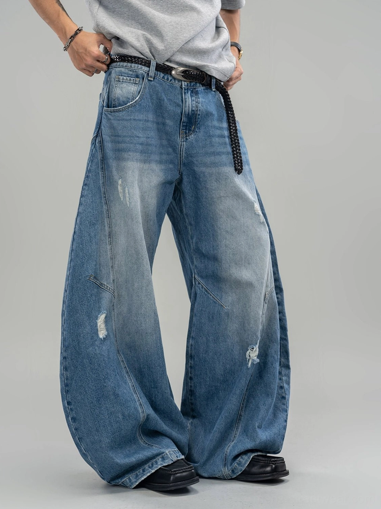 Close-up front view of faded blue ultra-wide streetwear jeans featuring front pockets knee tucks and distressed details