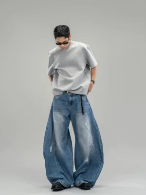 Front full-body view of distressed indigo ultra-wide balloon leg streetwear jeans styled with a grey t-shirt in a studio
