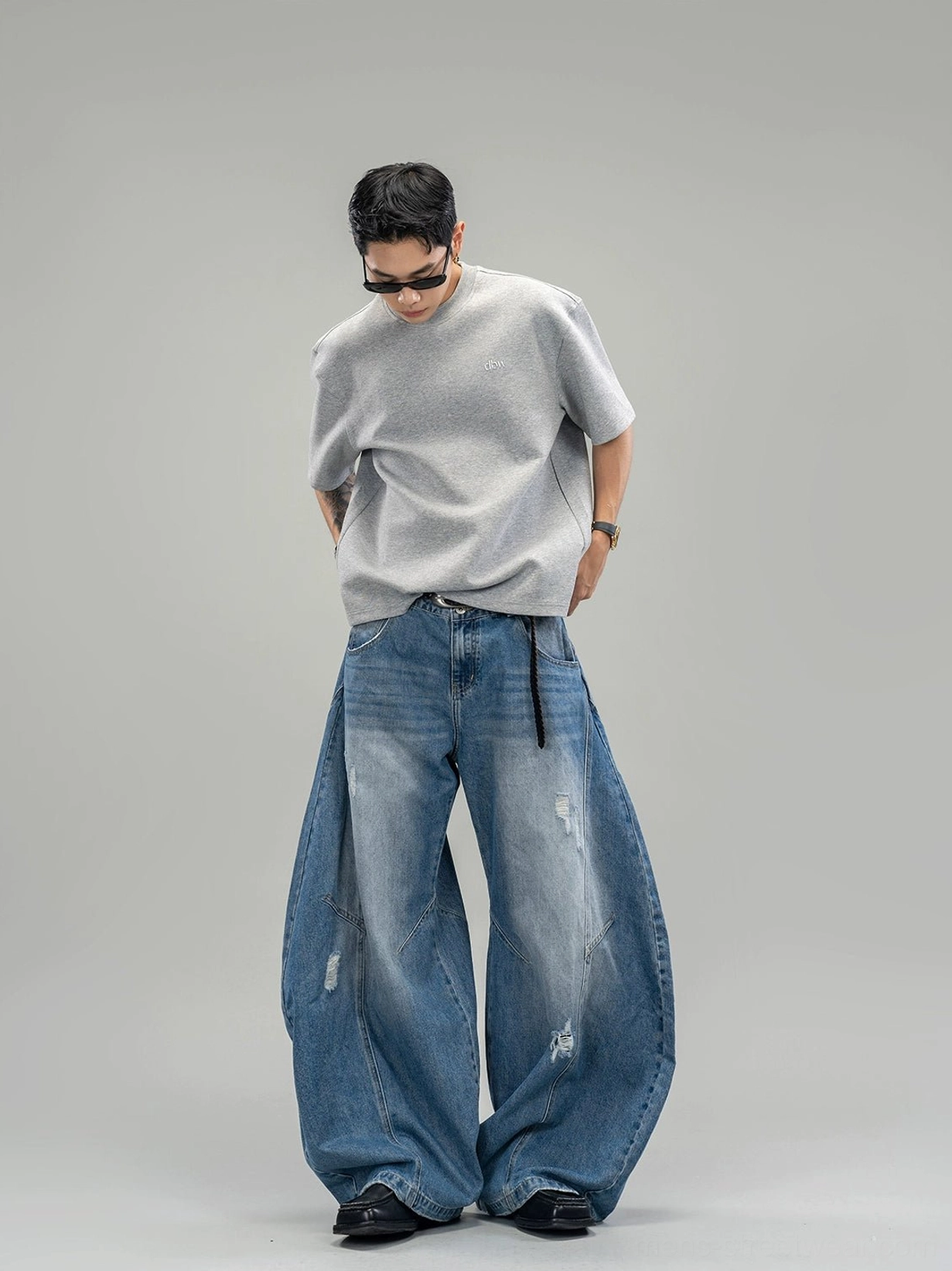 Front full-body view of distressed indigo ultra-wide balloon leg streetwear jeans styled with a grey t-shirt in a studio